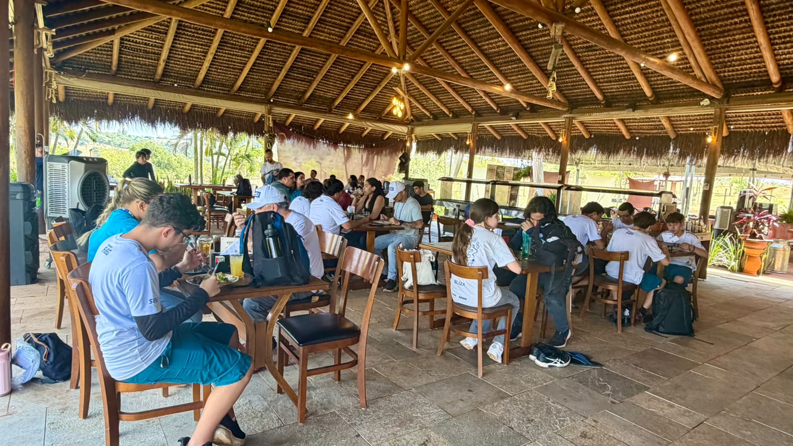 Estudantes almoçando no espaço coberto com mesas de madeira