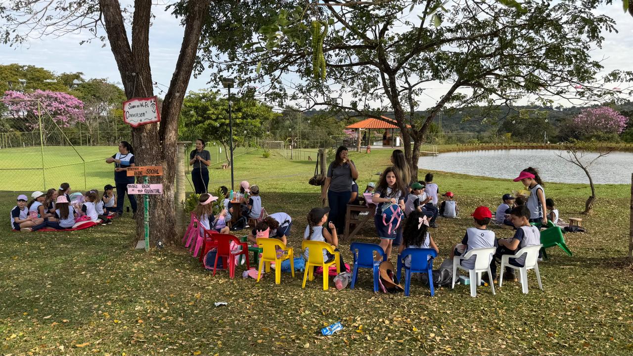 Turma reunida em roda de cadeiras coloridas sob as árvores